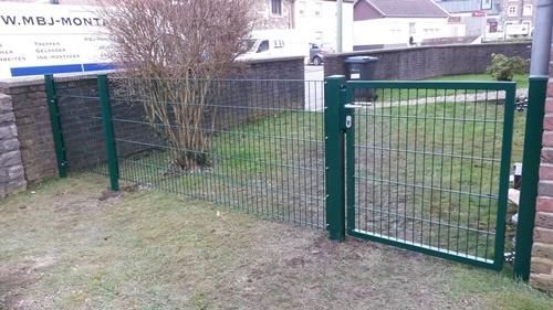 Ein grüner Zaun mit einem Tor und einem Schild im Hintergrund.