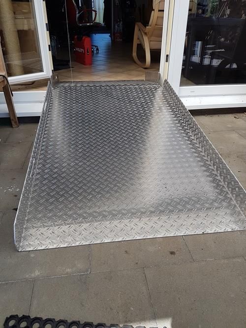 Eine Metallrampe, die zu einer Tür führt, im Hintergrund ein Stuhl