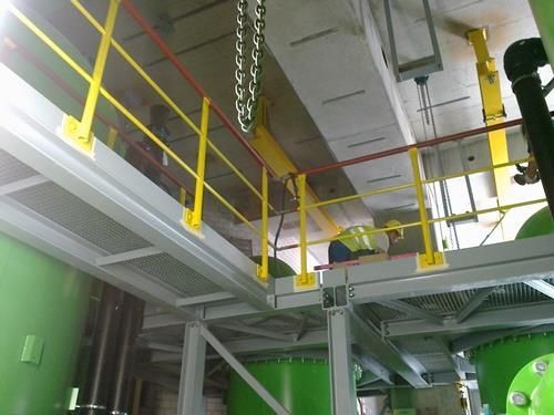 Ein gelbes Geländer in einer Fabrik mit grünen Tanks