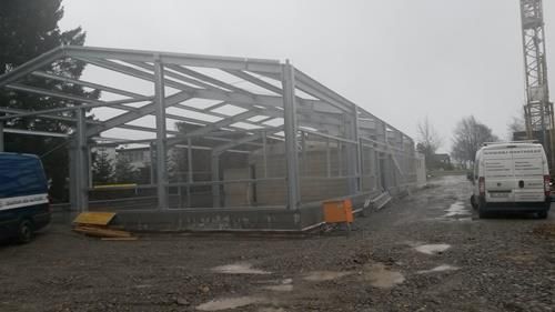 Ein im Bau befindliches Gebäude mit einem Kran im Hintergrund und vielen davor geparkten Autos.