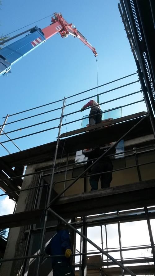 Ein Mann steht auf einem Gerüst und blickt zu einem Kran hoch.