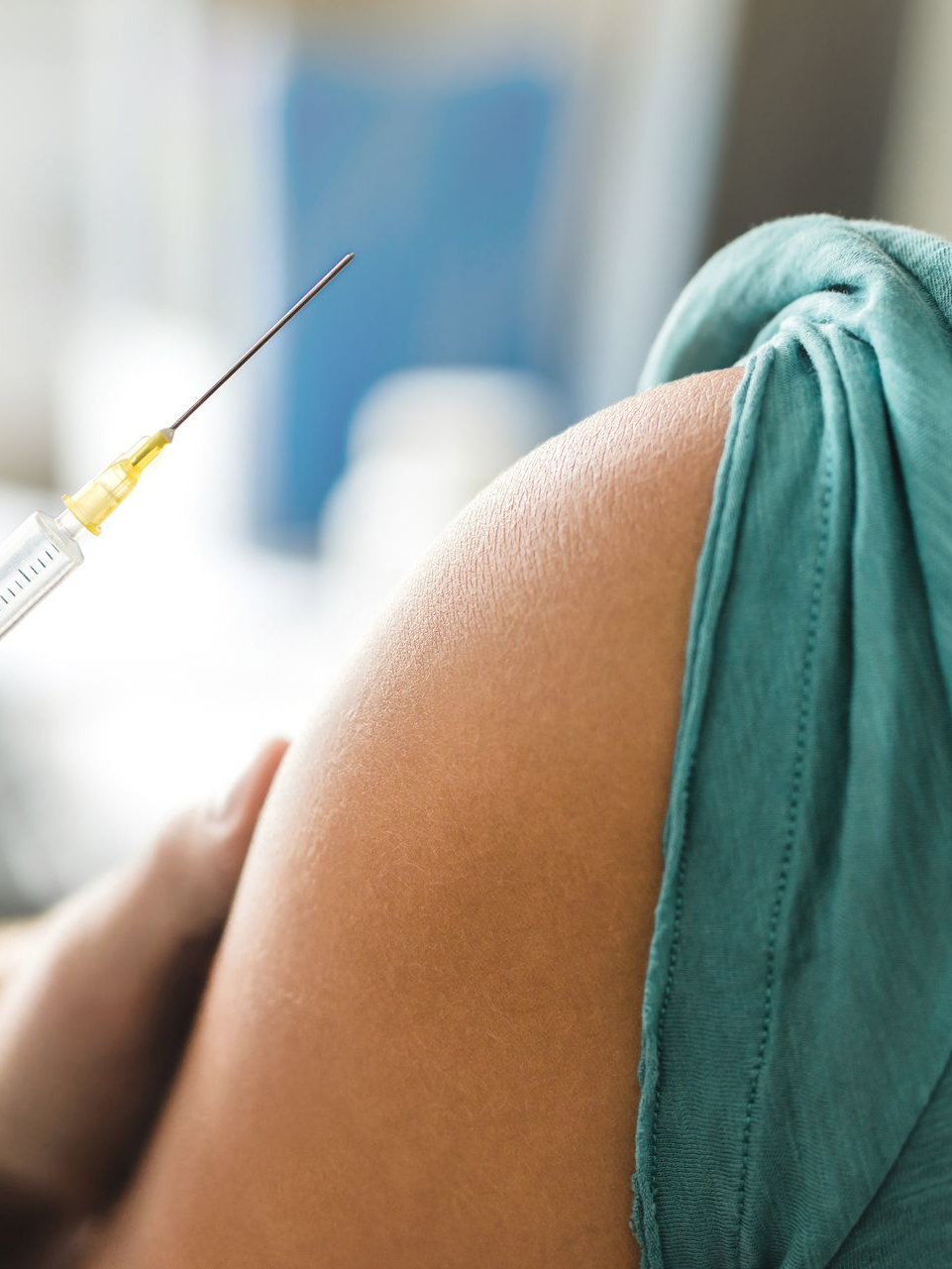 Une seringue injectant un vaccin dans le haut du bras d'une personne, recouverte d'une gaine turquoise.