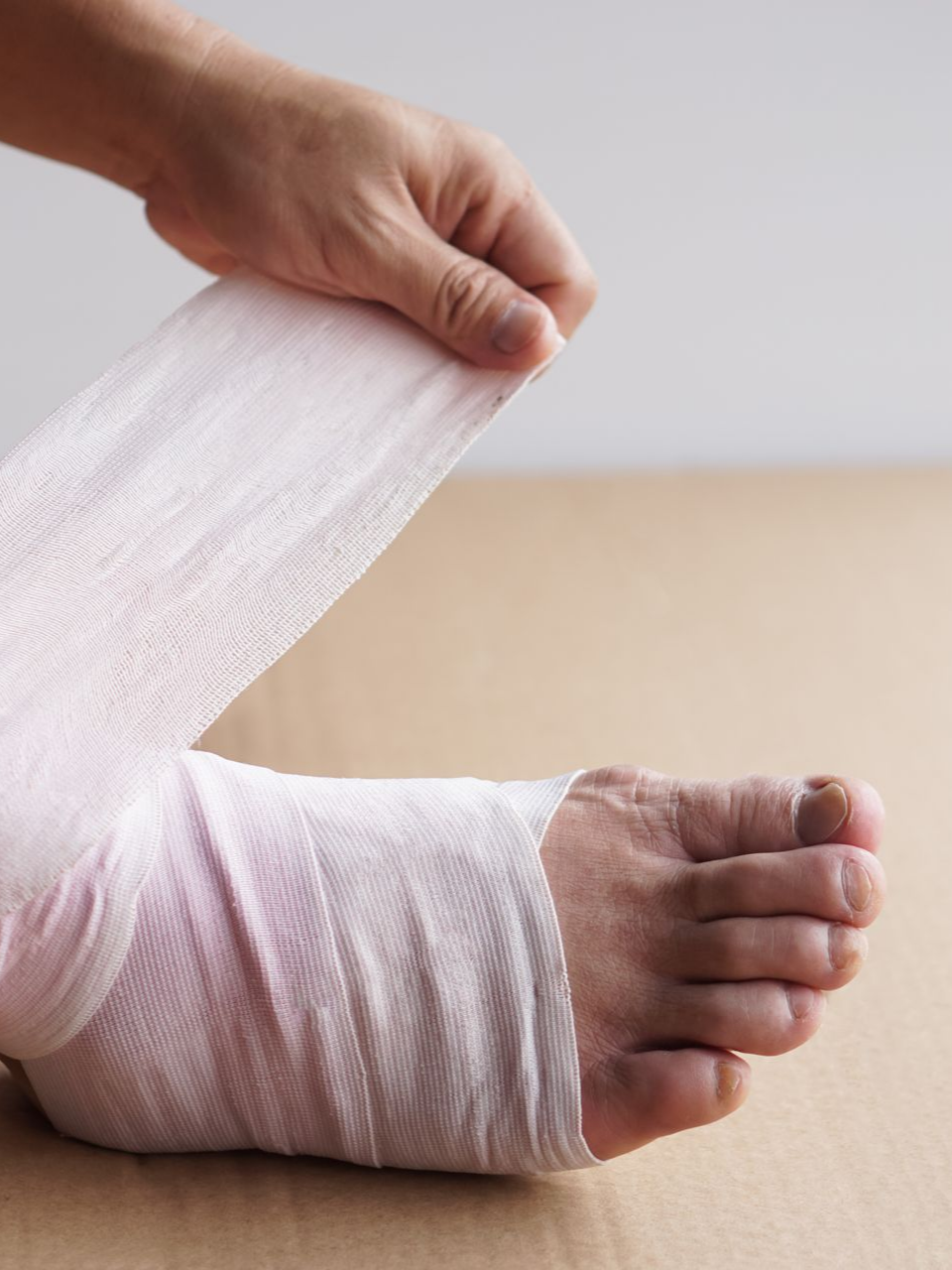Une personne enroule un bandage de gaze blanche autour du pied.