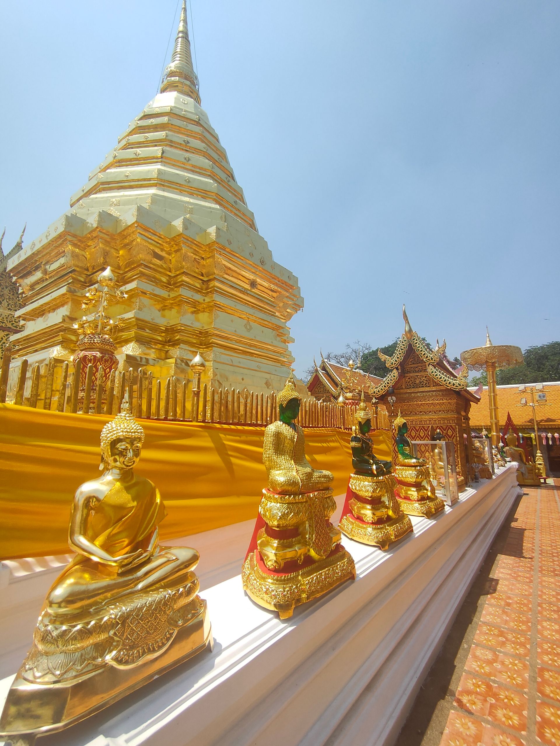Statues de Bouddha dorées devant un stupa de temple doré sous un ciel bleu