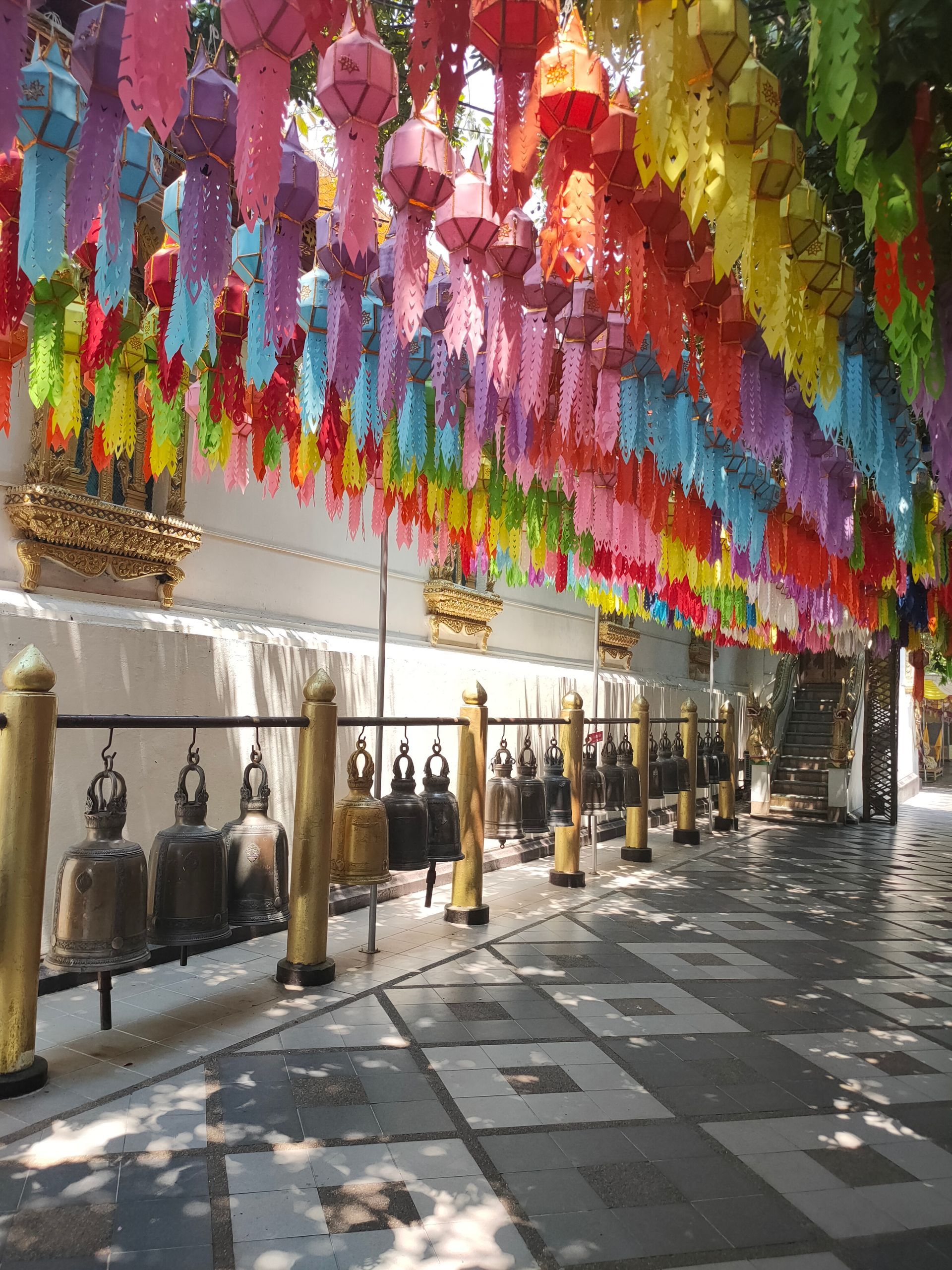 Des parasols et des lanternes colorés suspendus au-dessus d'une allée ombragée avec des balustrades et des carreaux à motifs