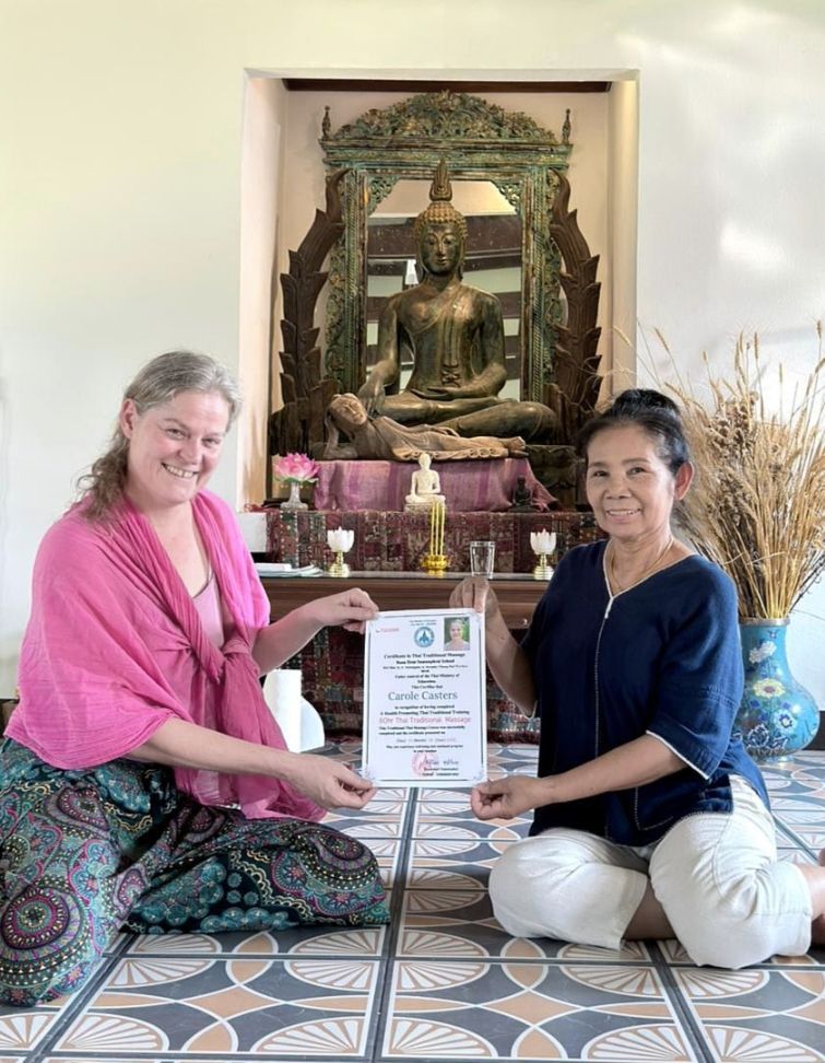 Deux femmes assises à l'intérieur tiennent un certificat encadré devant une statue de Bouddha et un autel.