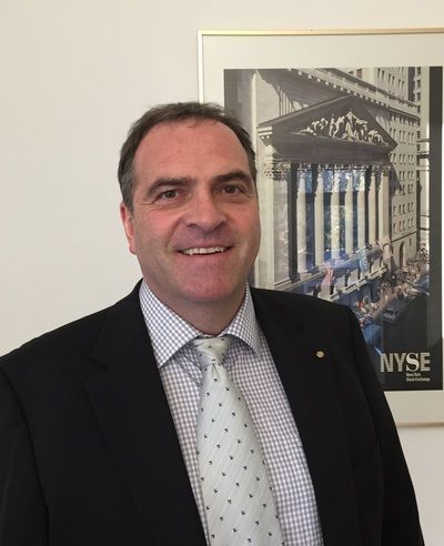 Ein Mann im Anzug lächelt neben einem gerahmten Bild des NYSE-Gebäudes.