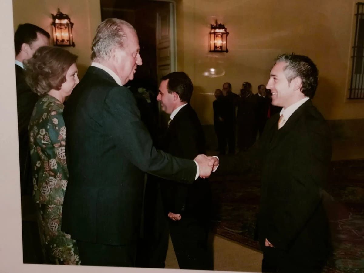 El Rey Juan Carlos y la Reina Sofía de España estrechan la mano de un hombre durante un evento formal en un lugar cerrado.