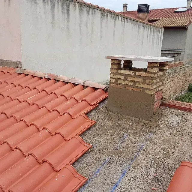 Un techo con tejas rojas y una chimenea encima.