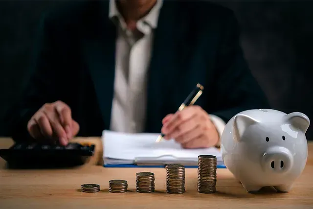 Un hombre está sentado en una mesa con una alcancía y montones de monedas.