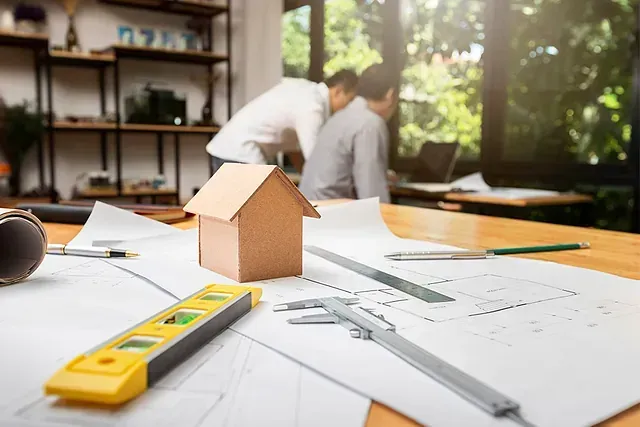 Una casa modelo está colocada encima de una mesa de madera al lado de una regla y un calibrador.