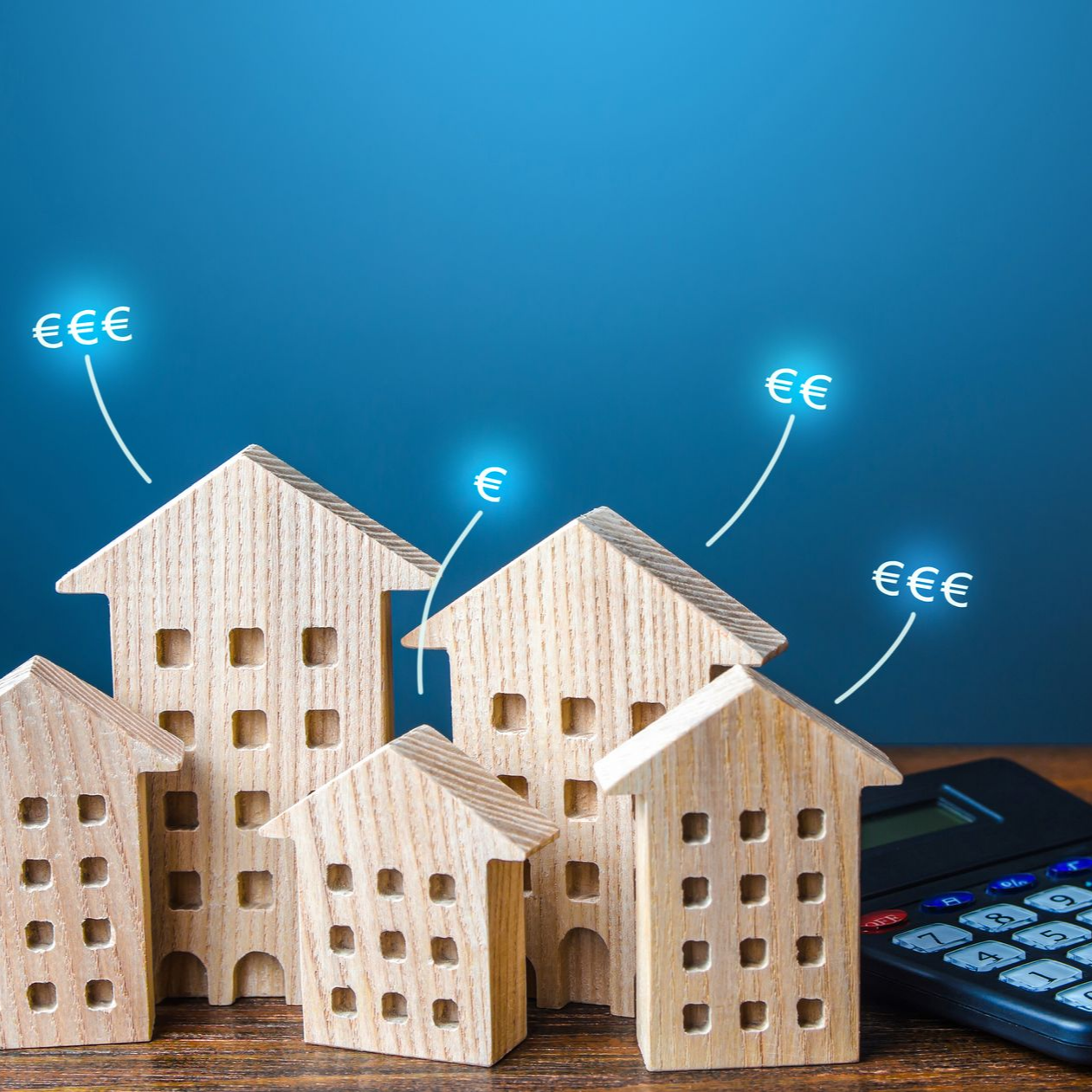 Maquettes de maisons avec une calculatrice et des symboles monétaires bleus en euros.
