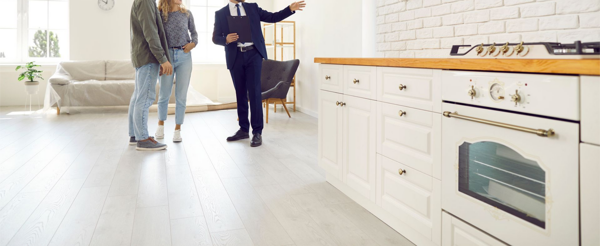 Un agent immobilier fait visiter un salon ouvert sur la cuisine à un couple.