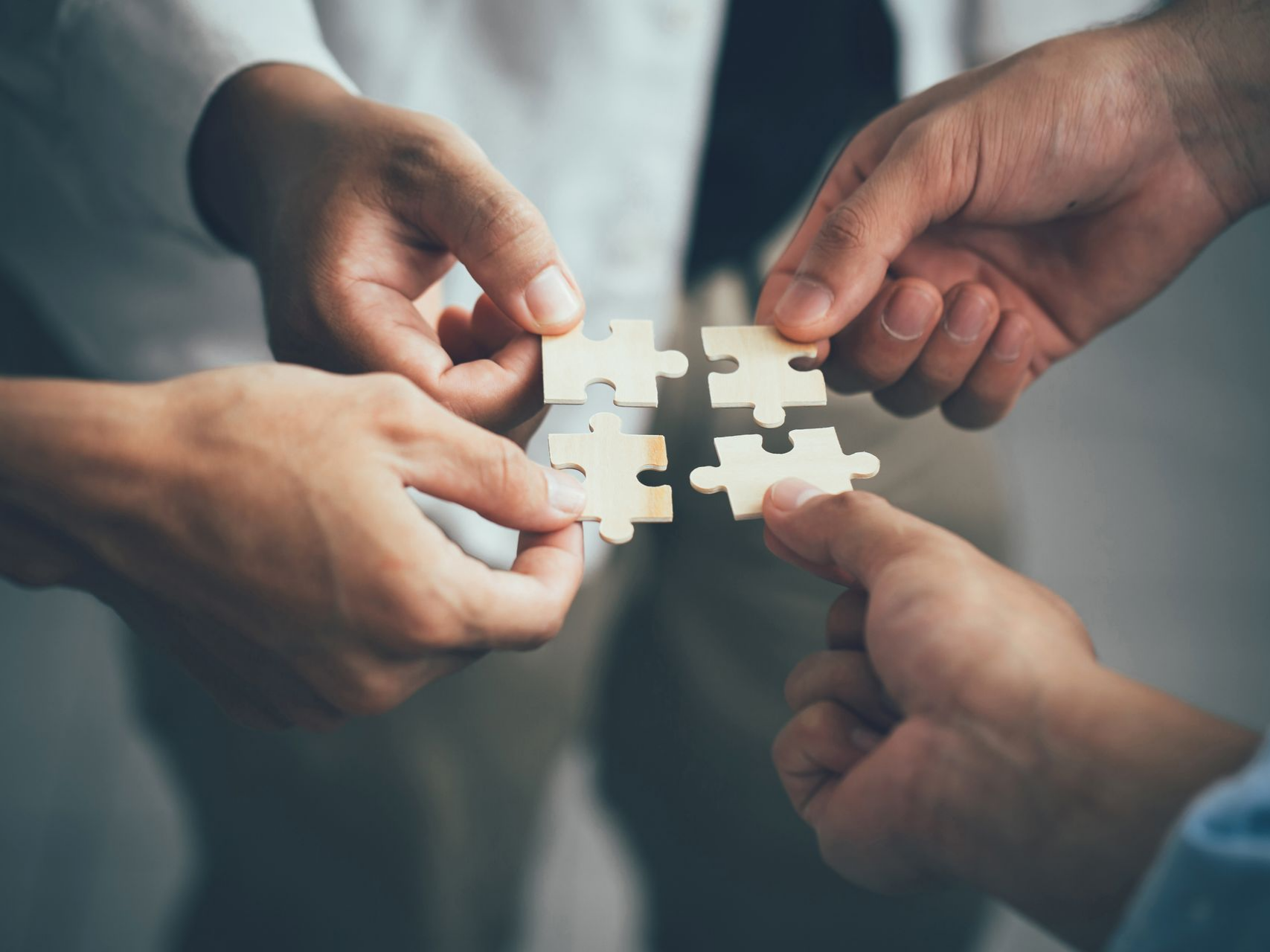 Quatre mains tenant ensemble quatre pièces de puzzle.