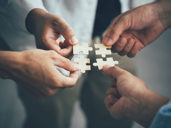 Vers la page Nos partenaires. Quatre mains tenant ensemble quatre pièces de puzzle.