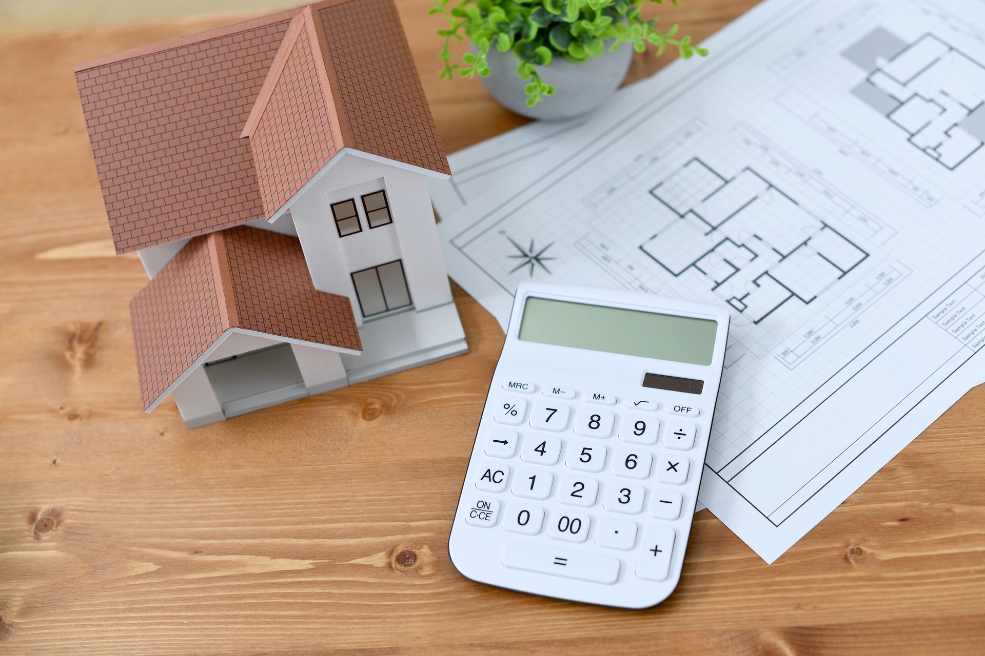 Une maquette de maison miniature est posée à côté d'une calculatrice et de plans architecturaux.