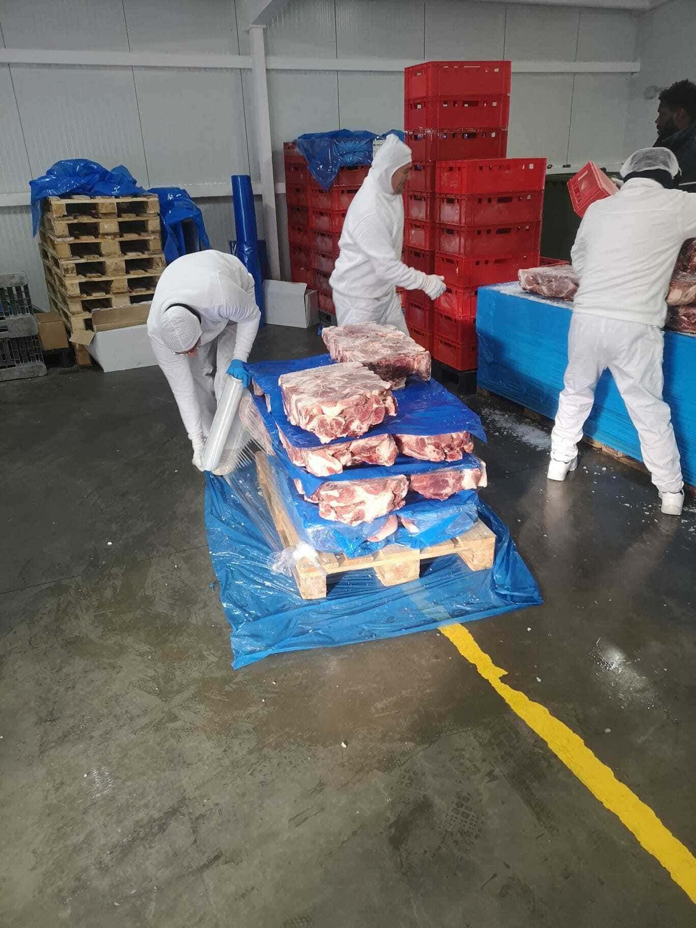 Un grupo de personas está trabajando en un palé de carne en un almacén.