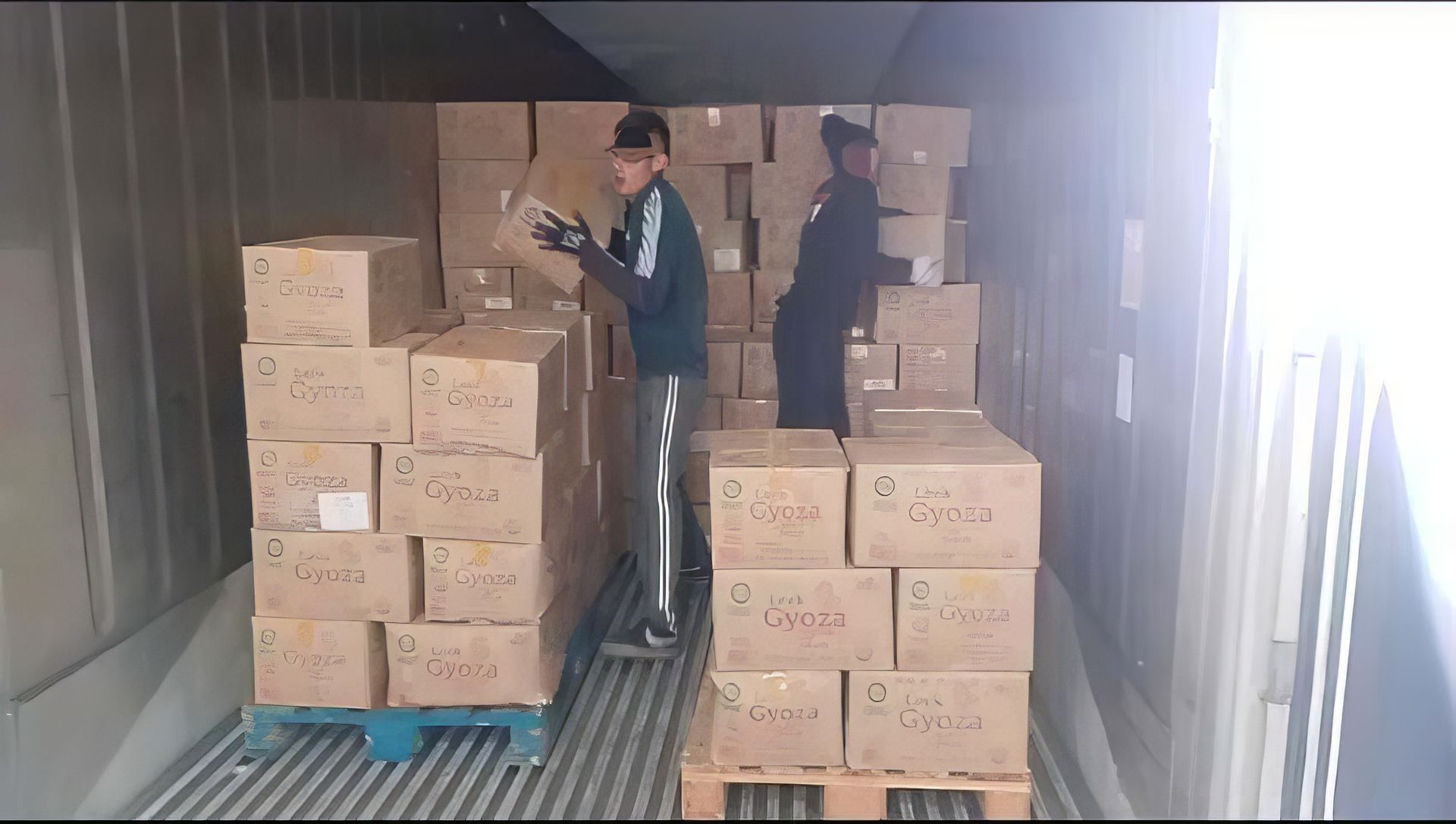 Dos hombres están cargando cajas en un contenedor de envío.