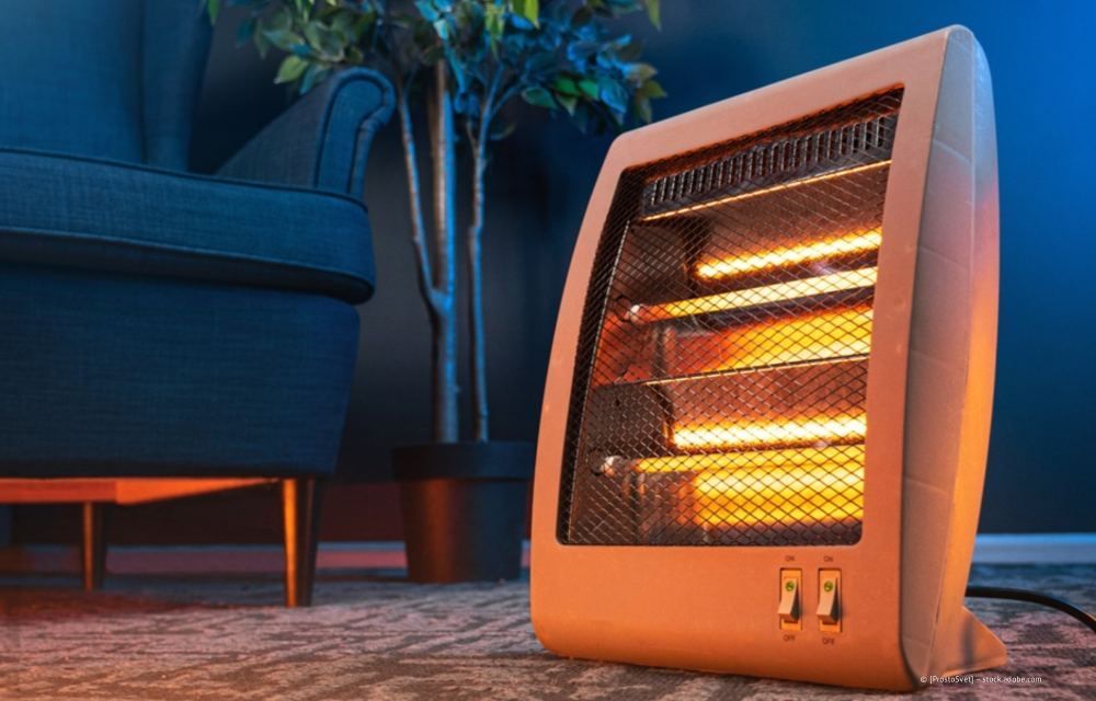 Ein kleiner, tragbarer Heizlüfter leuchtet orange neben einem Sofa in einem gemütlichen Wohnzimmer.