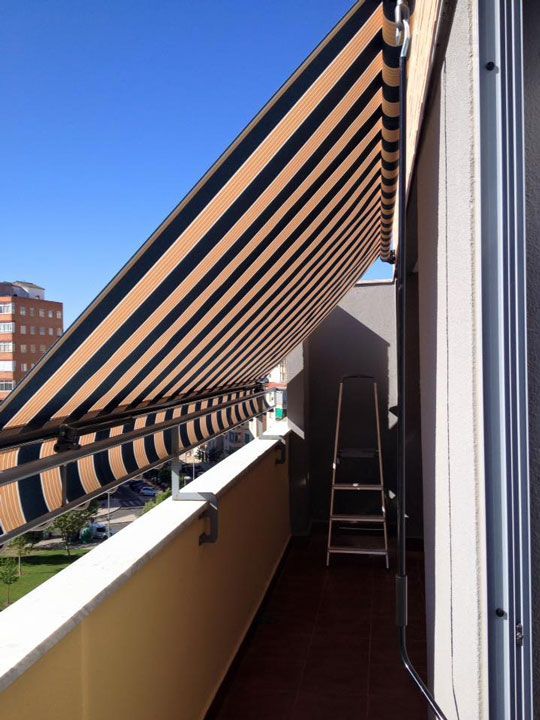 Un balcón con un toldo de rayas y una escalera.