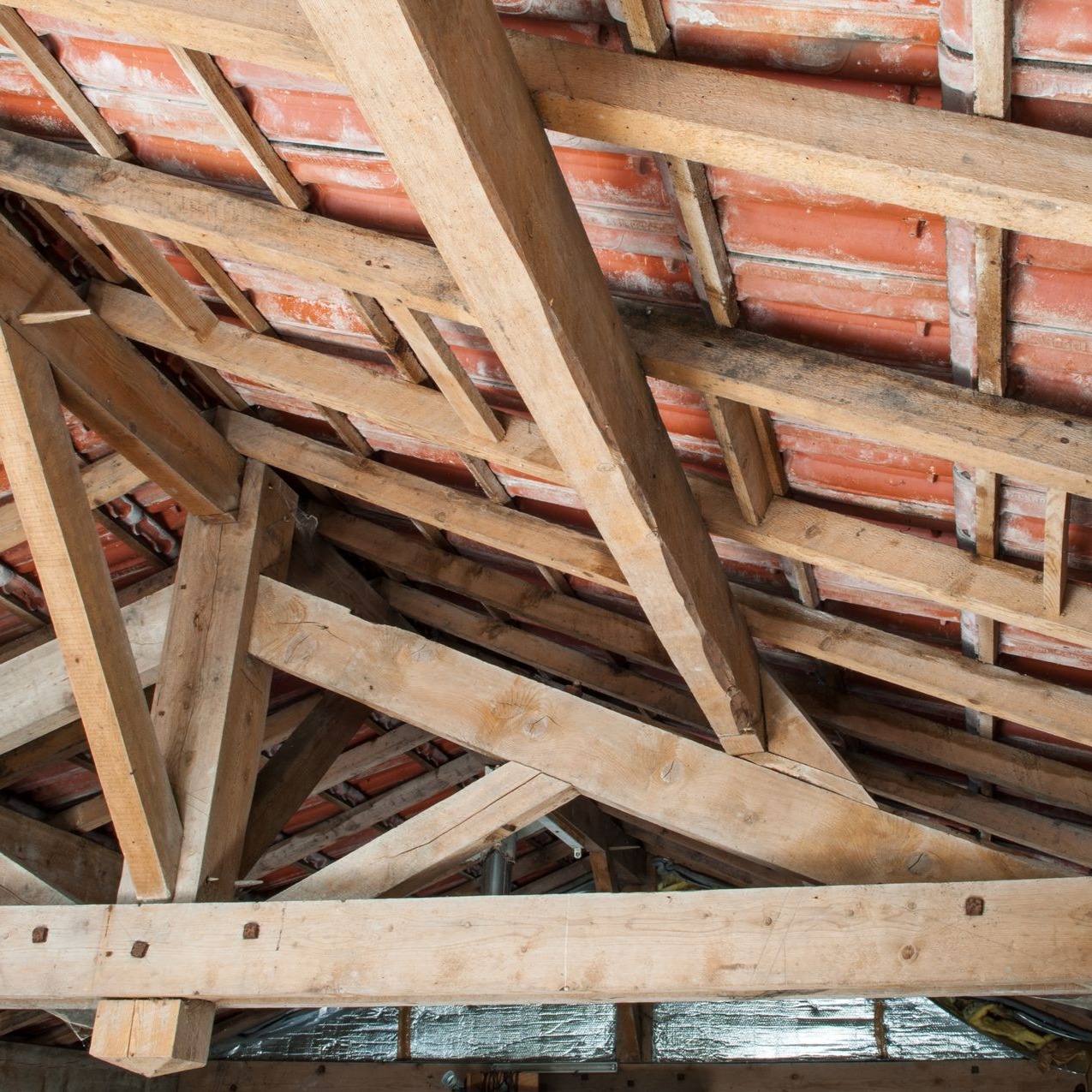 Chevrons de toit en bois supportant des tuiles en terre cuite.
