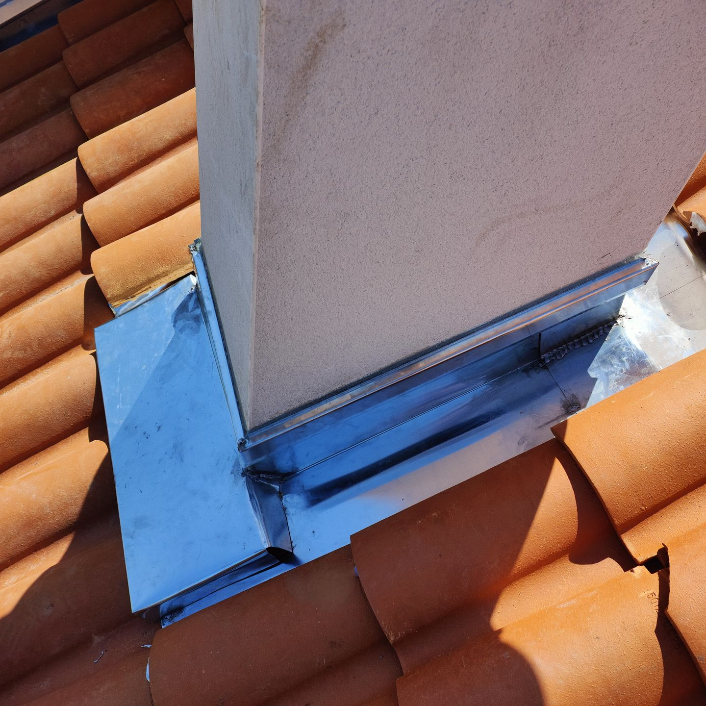 Cheminée sur toit en tuiles avec solin. Métal gris et tuiles en terre cuite.