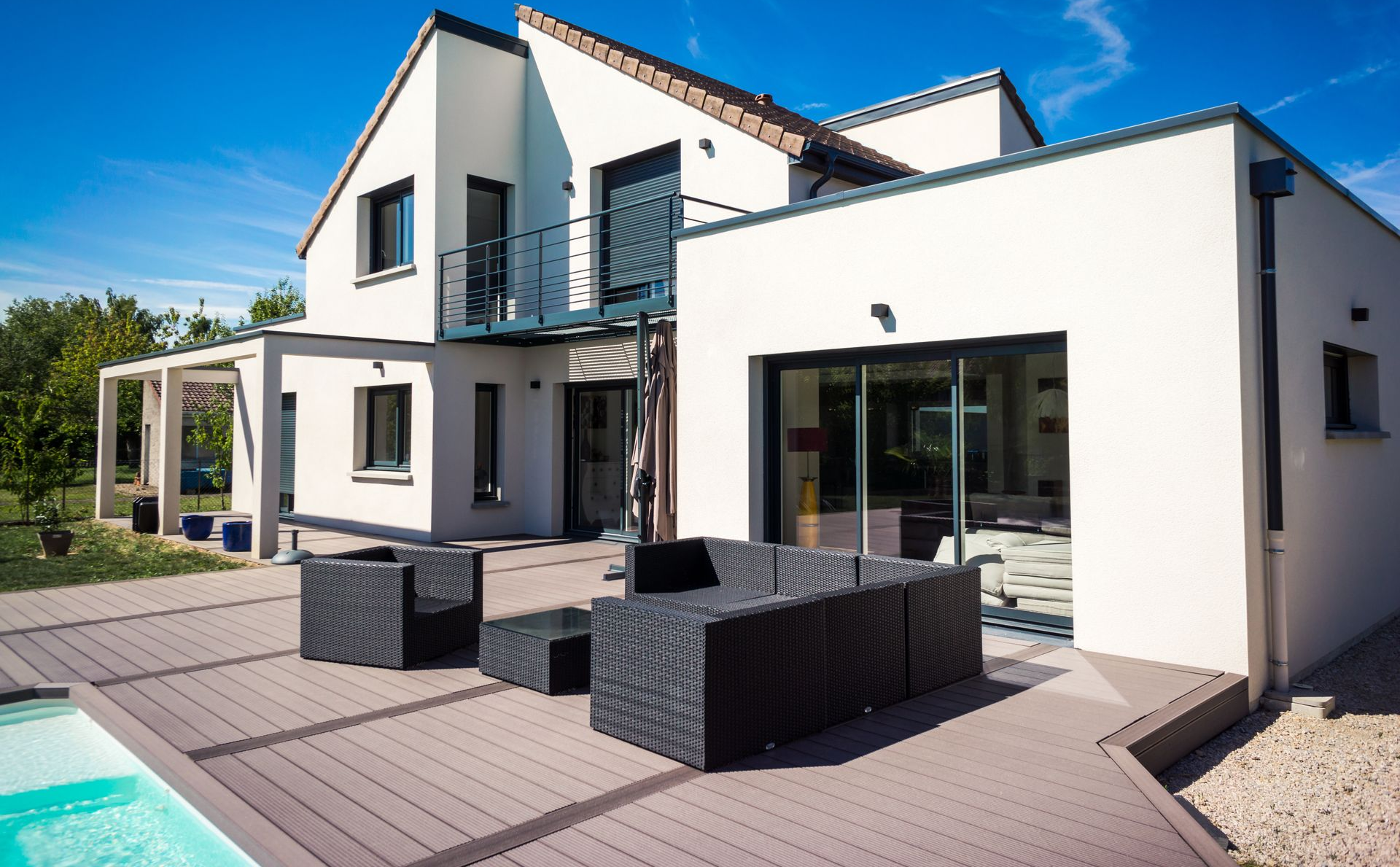 Maison blanche moderne avec garniture gris foncé, patio et piscine par une journée ensoleillée.