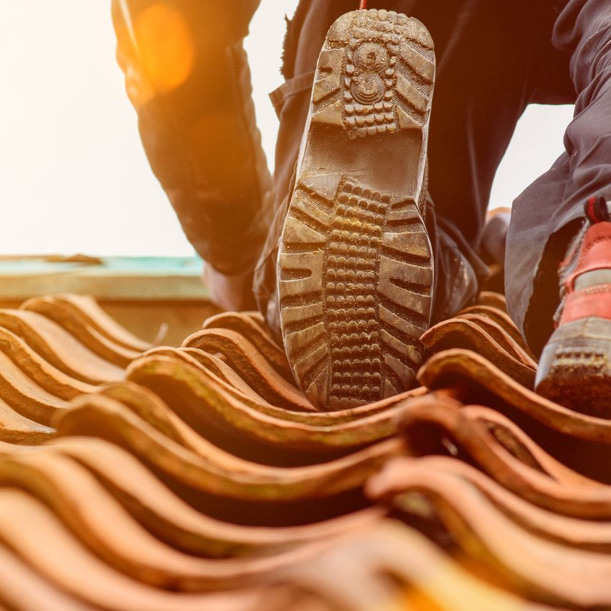 Une personne sur un toit avec une botte de travail marche sur un toit en tuiles en terre cuite, avec une perspective rapprochée.