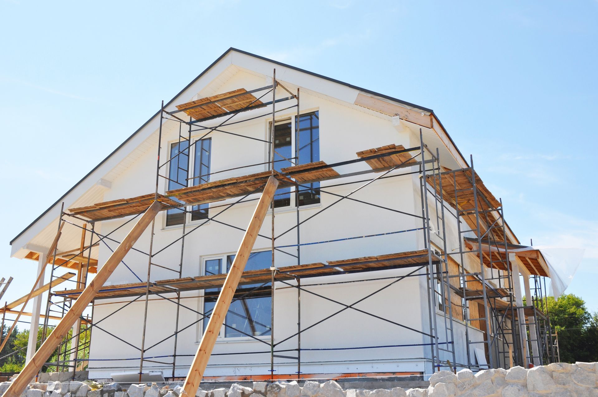 Maison en construction ; extérieur blanc, échafaudage, ciel bleu.