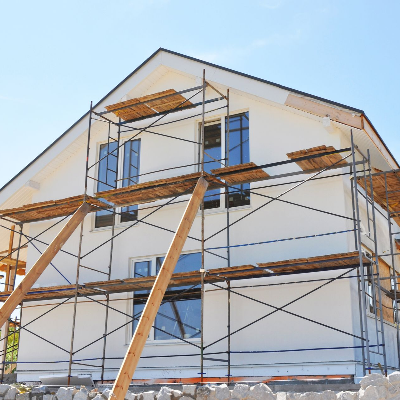 Maison en construction avec échafaudage contre murs en stuc blanc, ciel bleu.