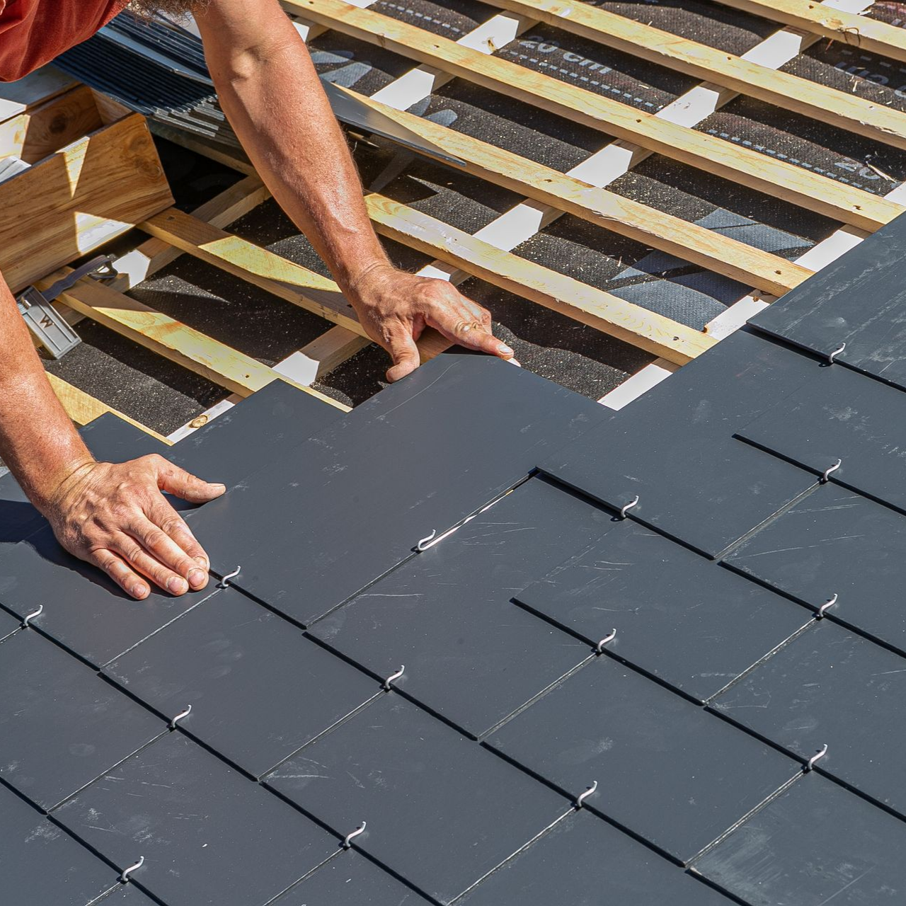 Personne installant des ardoises sur un toit à ossature en bois.