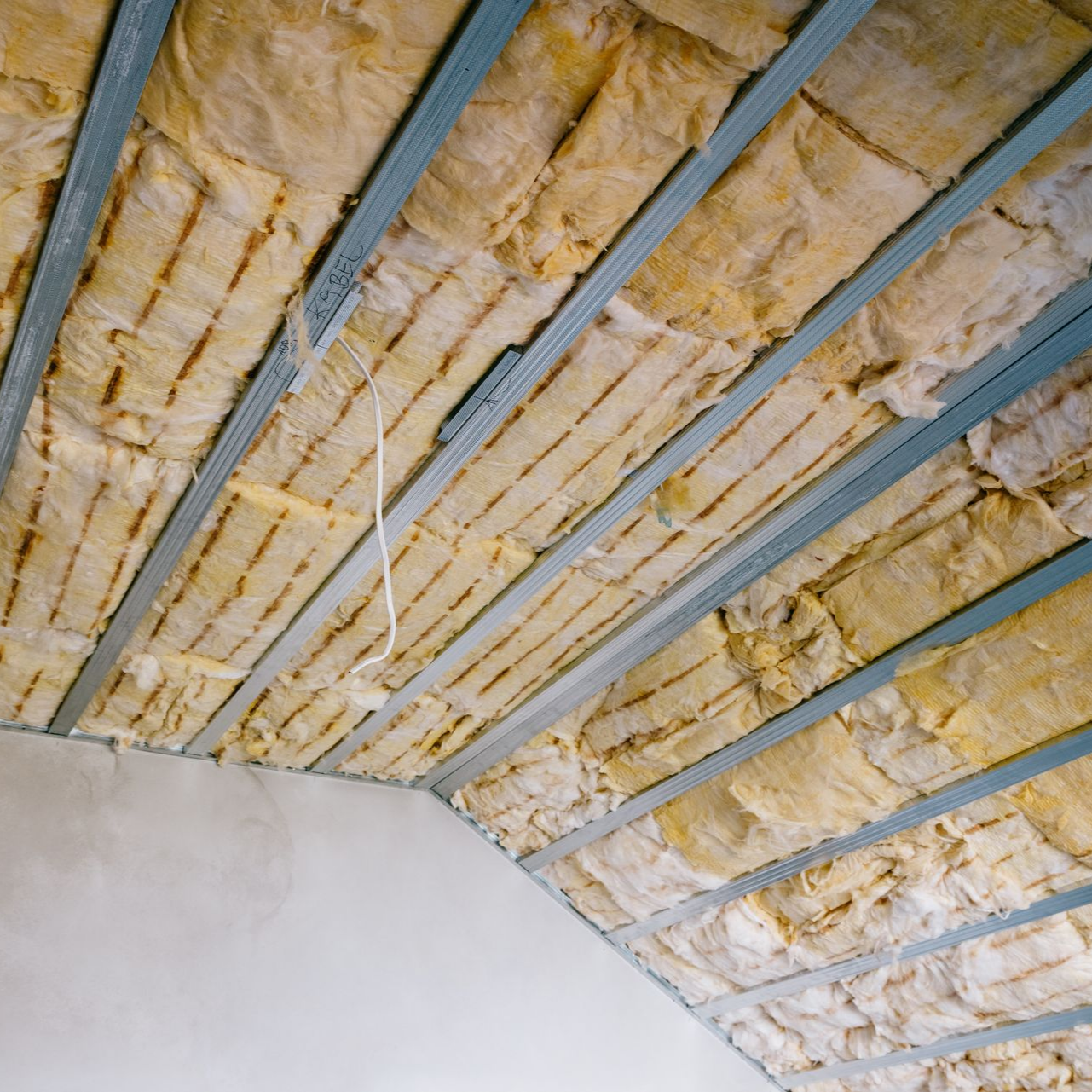 Plafond en construction, avec isolation jaune entre poutres métalliques.