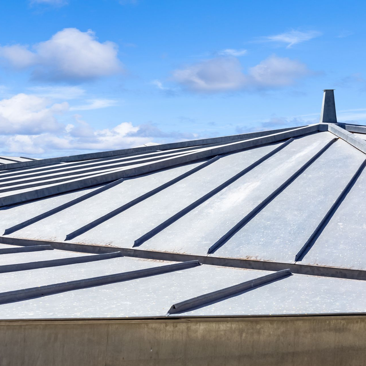 Toiture en métal gris avec des coutures surélevées contre un ciel bleu avec des nuages.