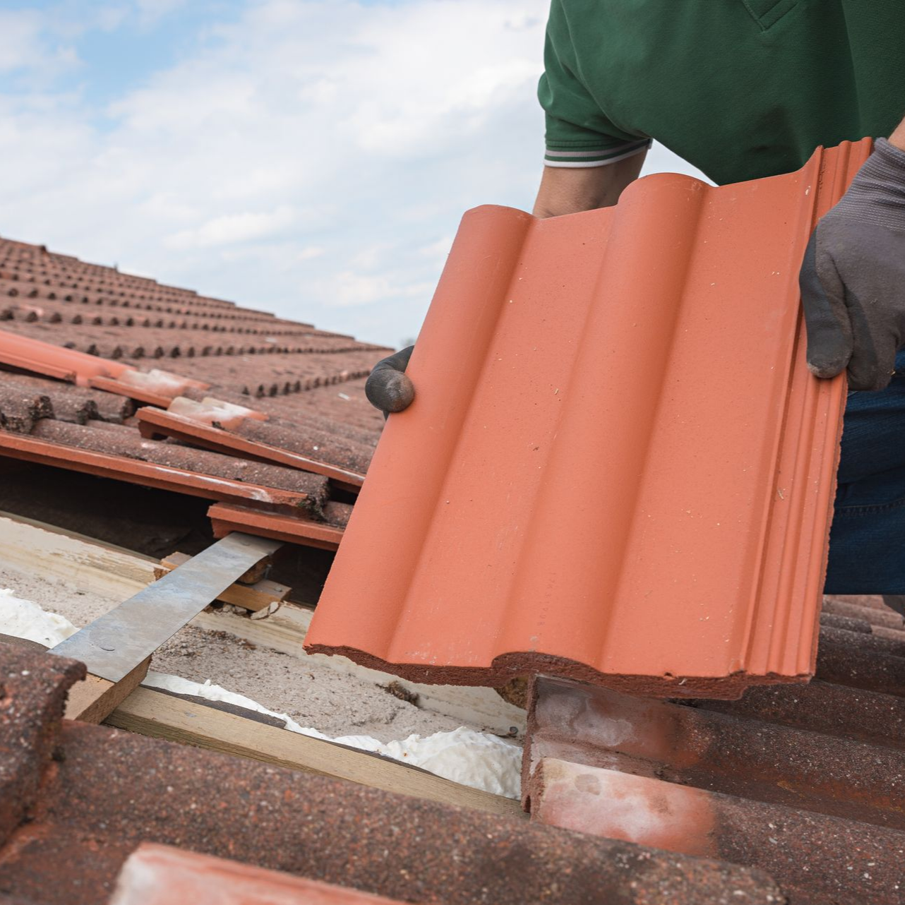 Une personne en chemise verte installe des tuiles en argile rouge par une journée ensoleillée.