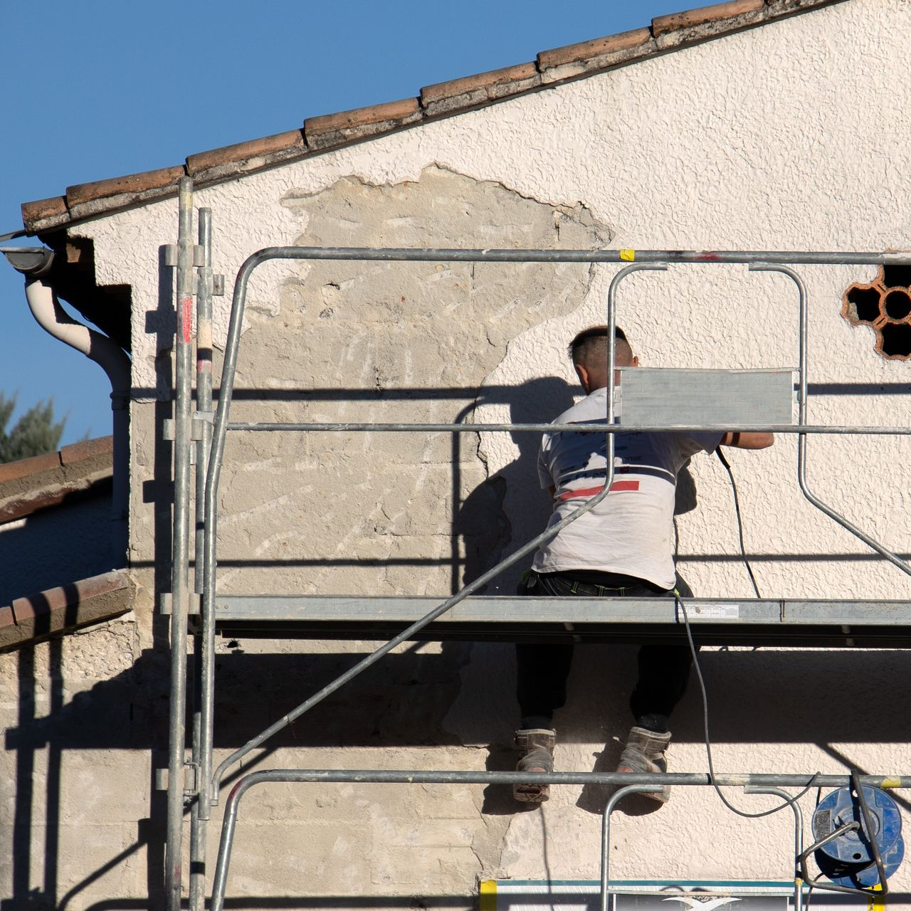 Un homme sur un échafaudage répare un mur en stuc.