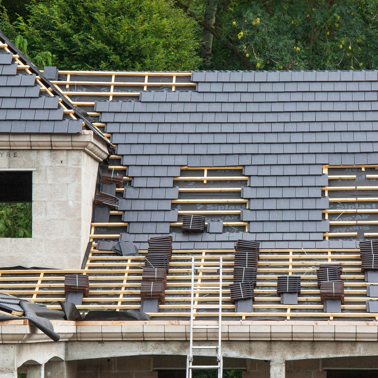 Toiture d'un bâtiment en construction, avec tuiles d'ardoise, poutres en bois et échelle.