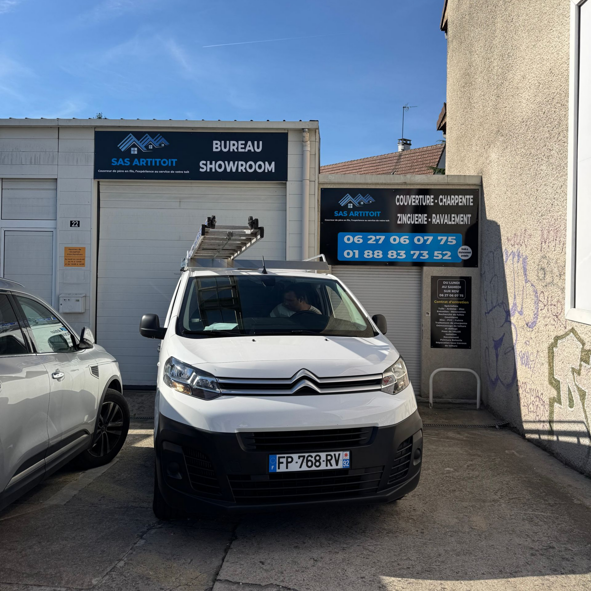 Toit en bardeaux gris avec un puits de lumière ; arbres en arrière-plan ; ciel au-dessus.