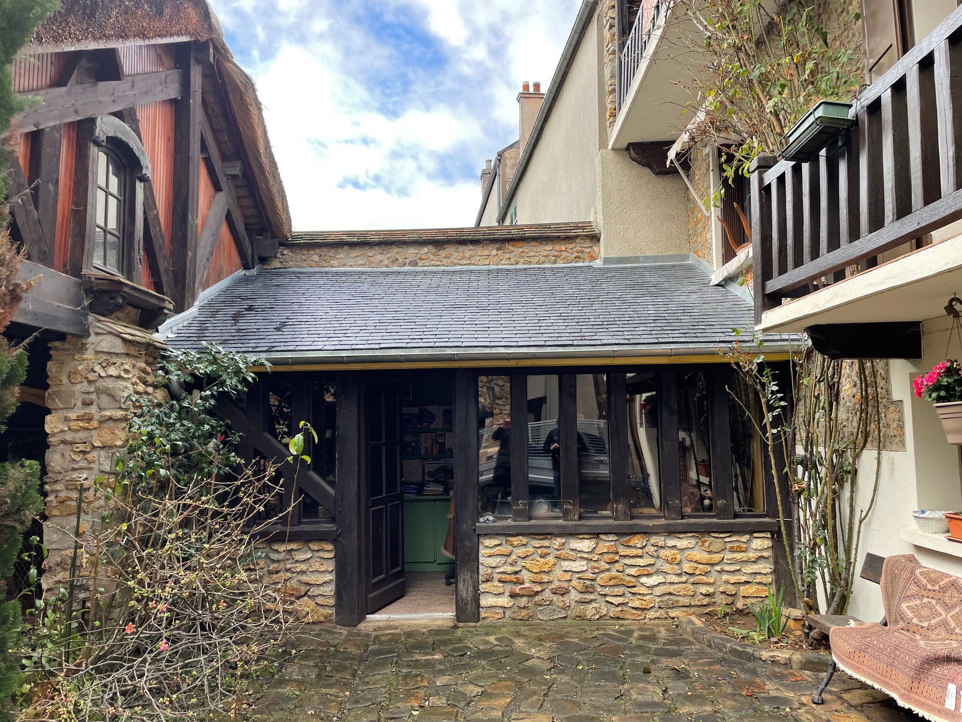 Bâtiment en pierre et à colombages avec un auvent en bois au-dessus d'une porte, ciel nuageux.