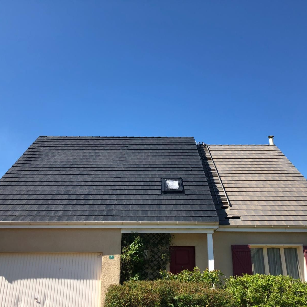 Maison avec un toit gris foncé fraîchement recouvert de bardeaux à gauche et gris délavé à droite ; ciel bleu.