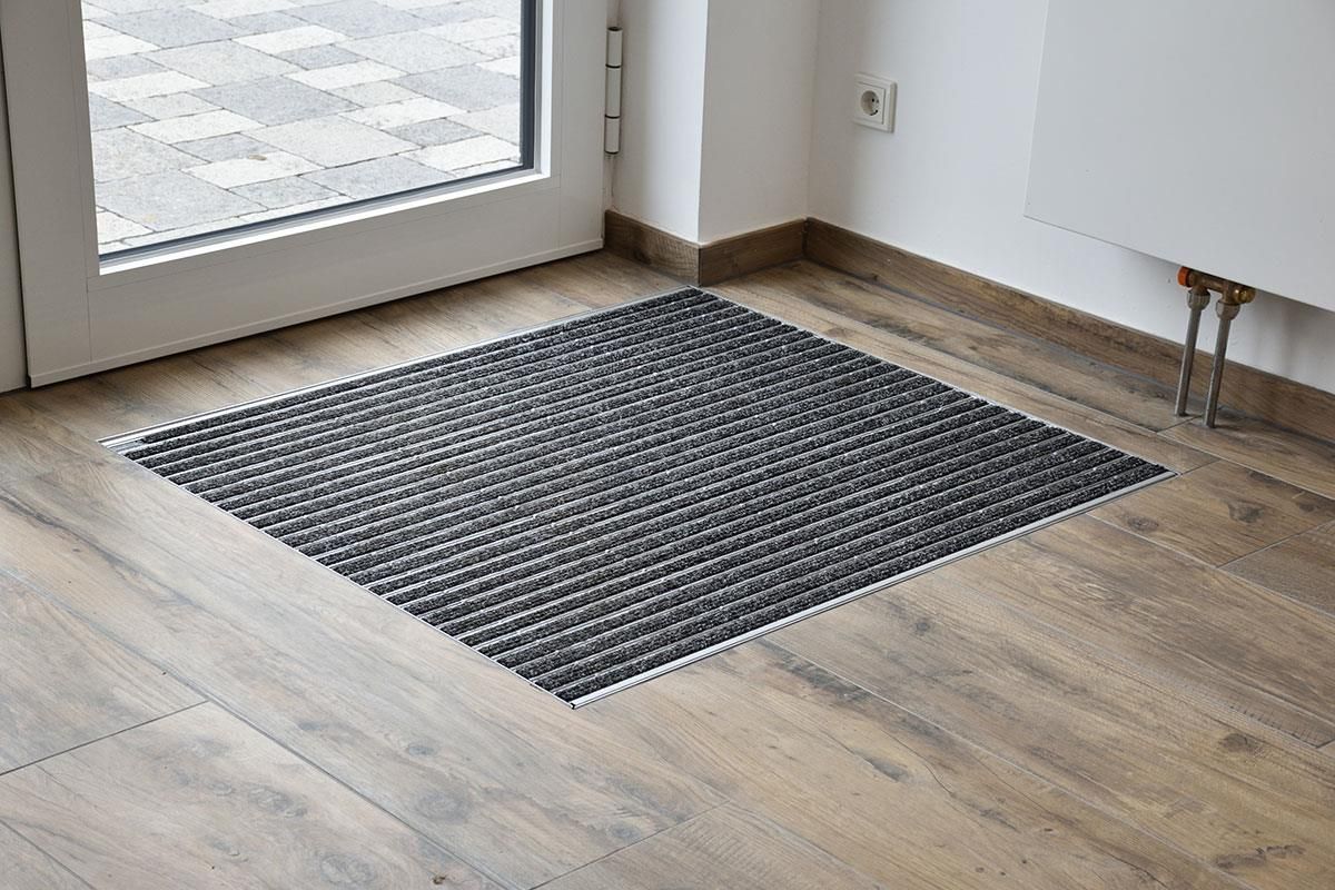 Auf einem Holzboden neben einem Fenster liegt eine Fußmatte.