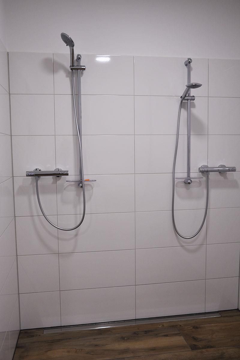 An einer weiß gefliesten Wand in einem Badezimmer hängen zwei Duschköpfe.