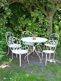Table et chaises de patio en fer forgé blanc sur l'herbe, sous un arbre feuillu.