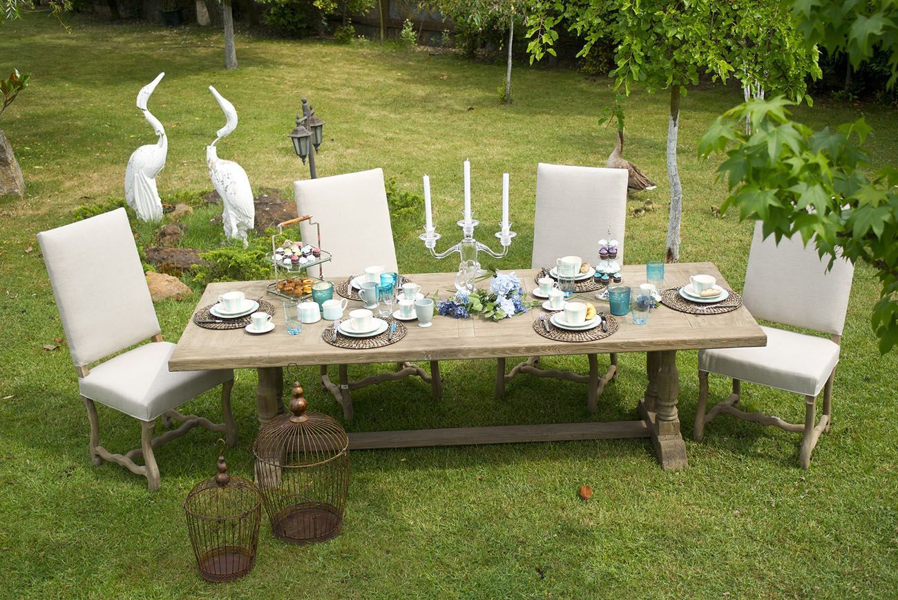 Ensemble de table et chaises blanches pour les repas en plein air dans le jardin, avec assiettes, bougies et statuettes de cygnes décoratives sur la pelouse.