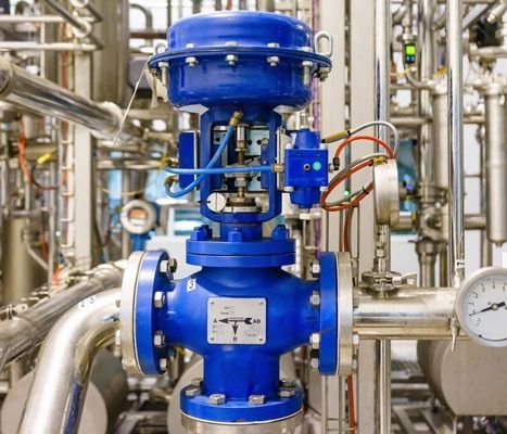 Una válvula azul está colocada encima de una tubería de metal en una fábrica.