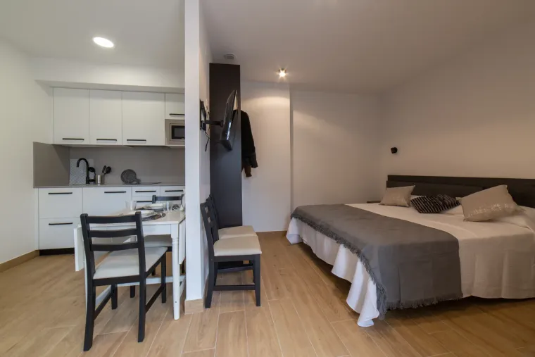 Apartamento tipo estudio con cocina, comedor y cama; paredes blancas, suelos de madera.