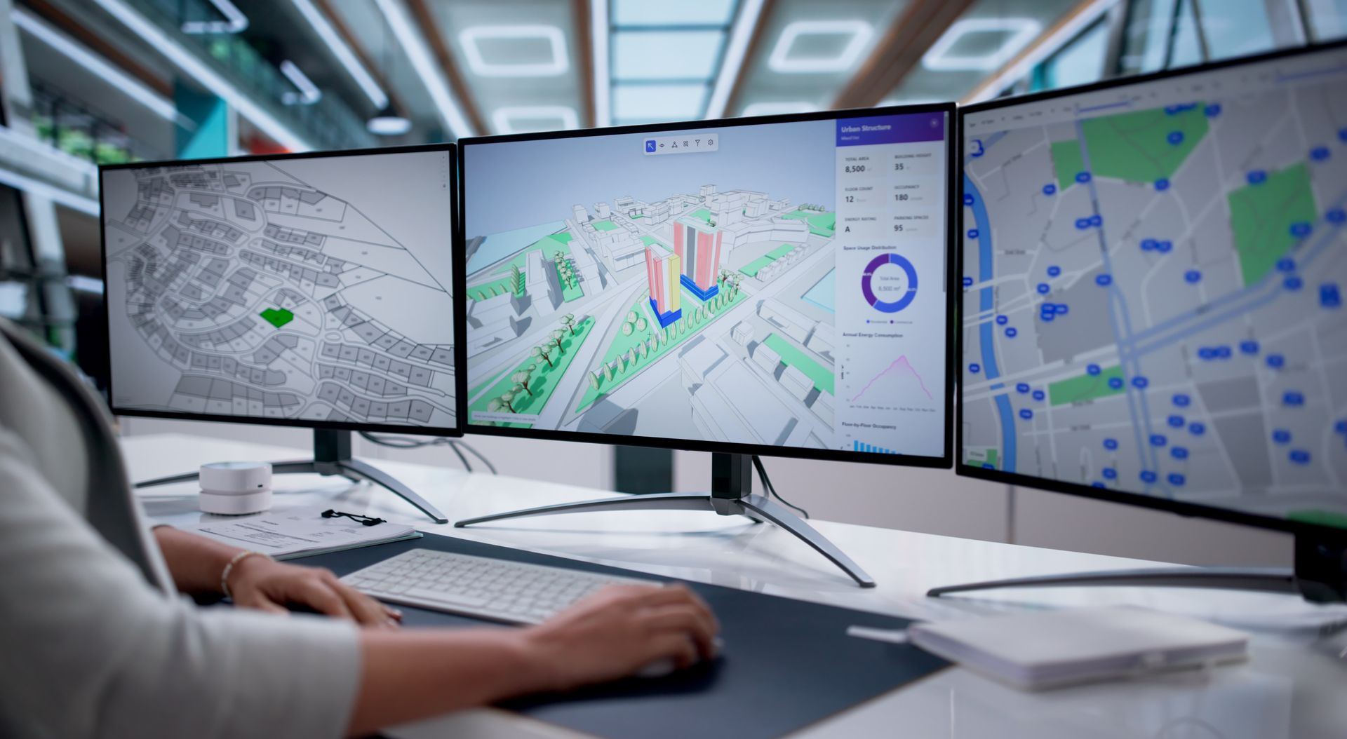 Une personne à son bureau utilise trois écrans affichant des cartes et des données.