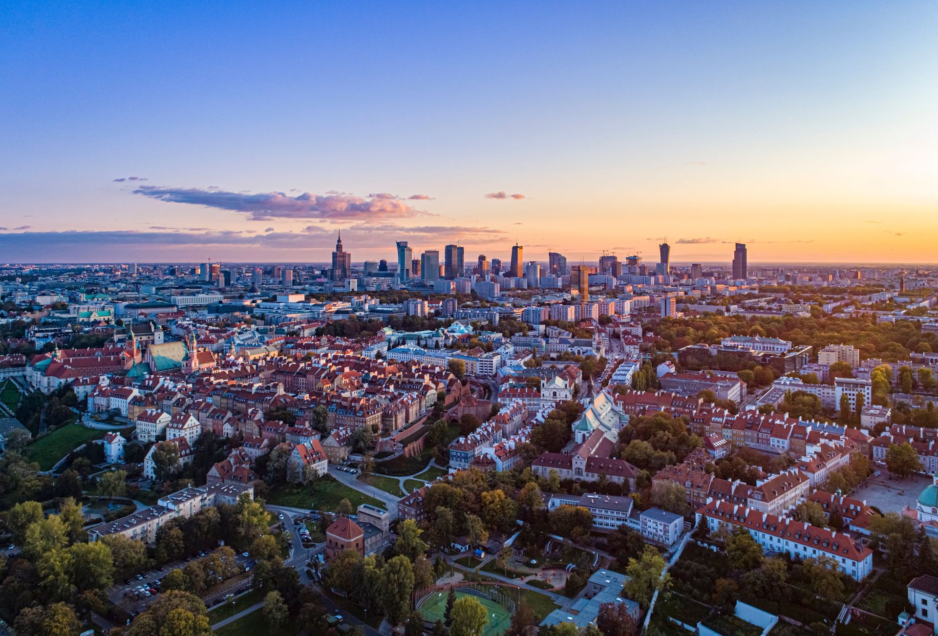 La silhouette d'une ville au coucher du soleil. Des immeubles de hauteurs variées se détachent sur un ciel coloré.