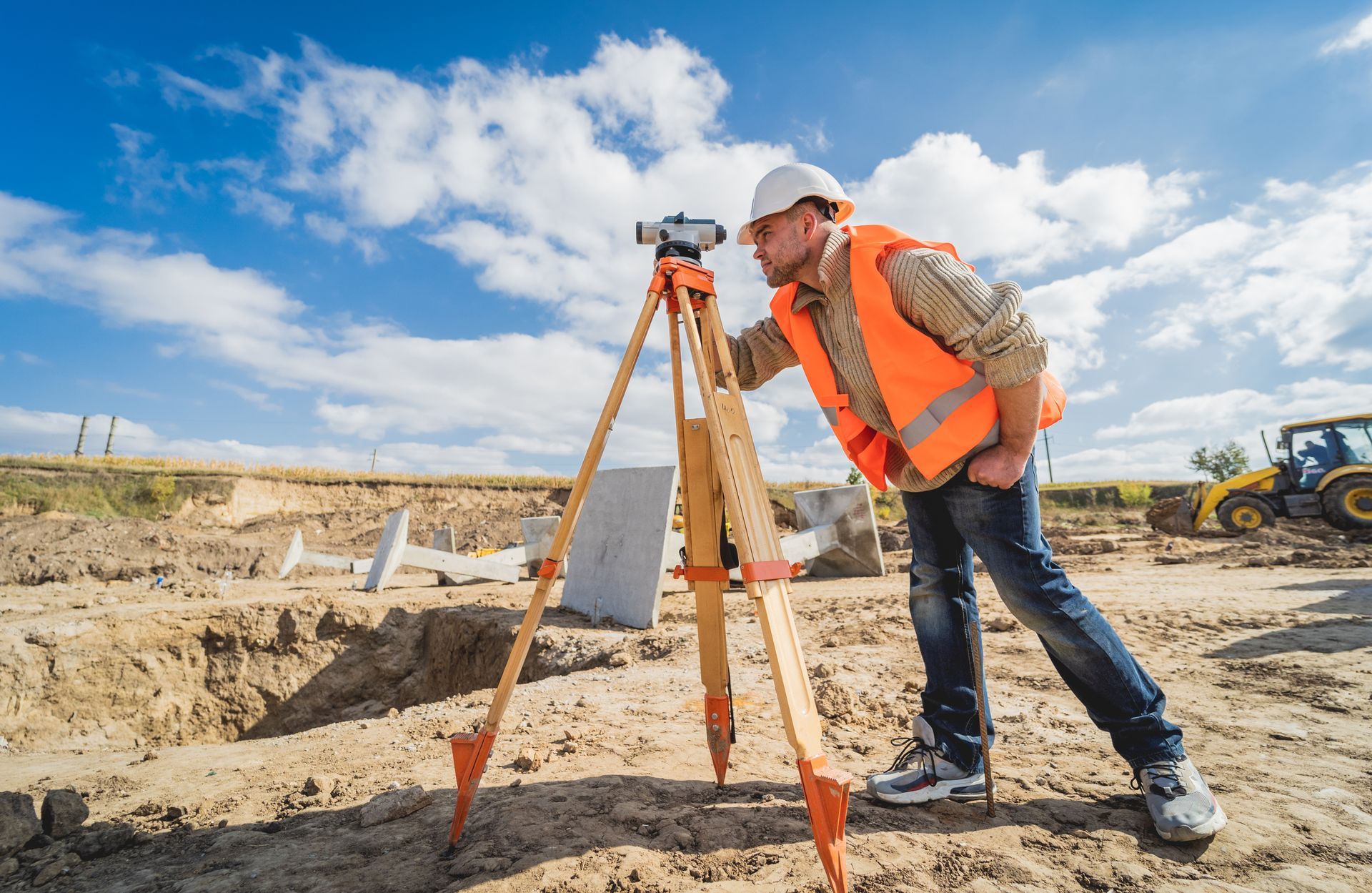 Géomètre utilisant un théodolite sur un chantier de construction ; ciel dégagé, gilet orange.
