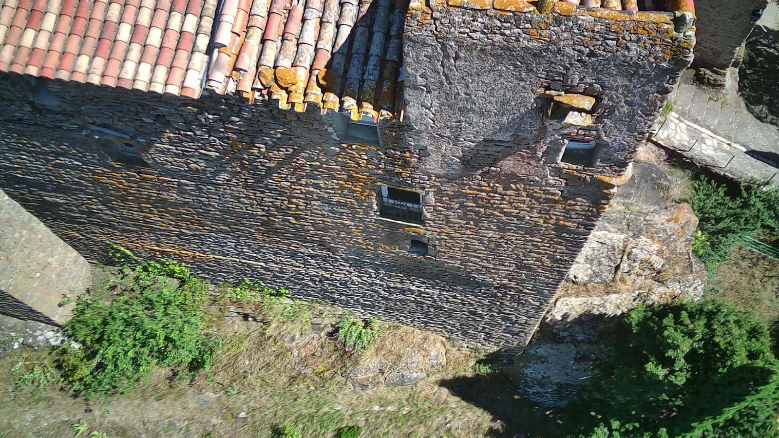 Vue aérienne d'un vieux toit en pierre recouvert de tuiles en terre cuite, de cheminées et de verdure environnante.