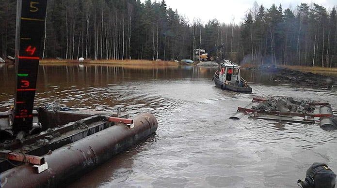Tulvanäkymä pienestä pelastusveneestä lähellä mutaista, turvonnutta joenpenkkaa ja tukkeja etualalla
